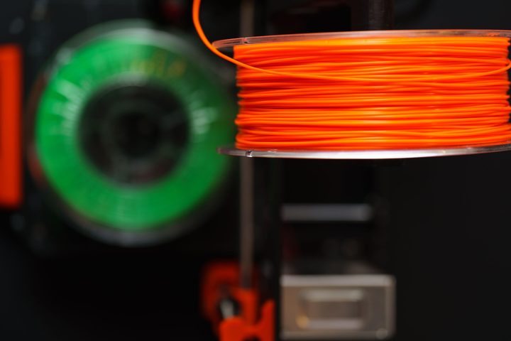 Orange 3D printer filament spool on a printer, with a green spool in the background